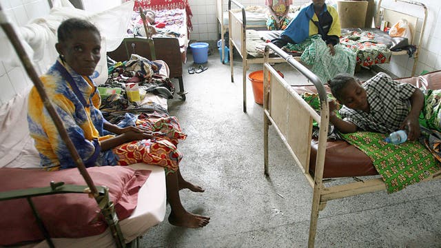 Foto eines Krankenzimmers mit altertümlichen Hospitalbetten, in denen Patientinnen mit ihren Habseligkeiten sitzen und liegen.