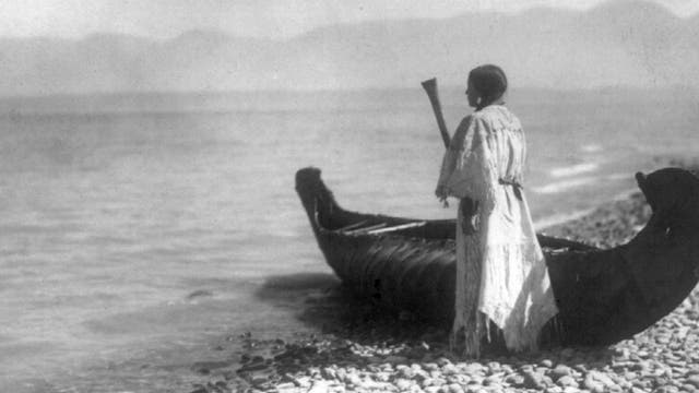 Eine Angehörige der Kutenai steht um 1910 neben einem Kanu in Nordamerika.
