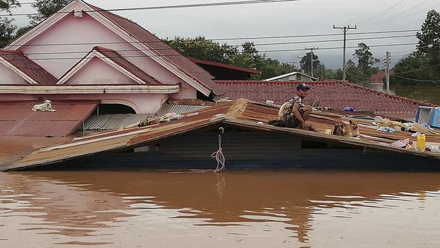 Ein Mensch sitzt auf dem Dach eines Hauses, das bis über die Fenster in schlammigem Wasser steht.