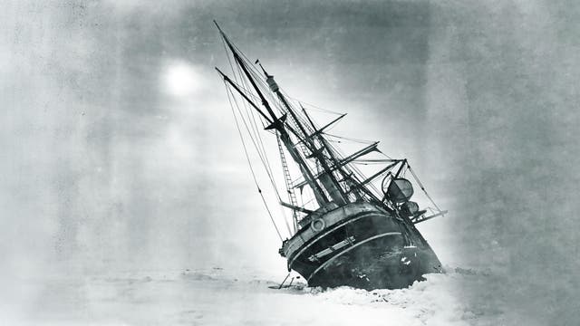 Ein historisches Schwarz-Weiß-Foto zeigt ein großes Segelschiff, das im Eis gefangen ist. Das Schiff ist zur Seite geneigt, umgeben von einer weiten, eisigen Landschaft. Der Himmel ist bewölkt, was die dramatische und herausfordernde Situation des Schiffes unterstreicht. Die Masten und Takelage sind deutlich sichtbar, was auf die Größe und Komplexität des Schiffes hinweist.