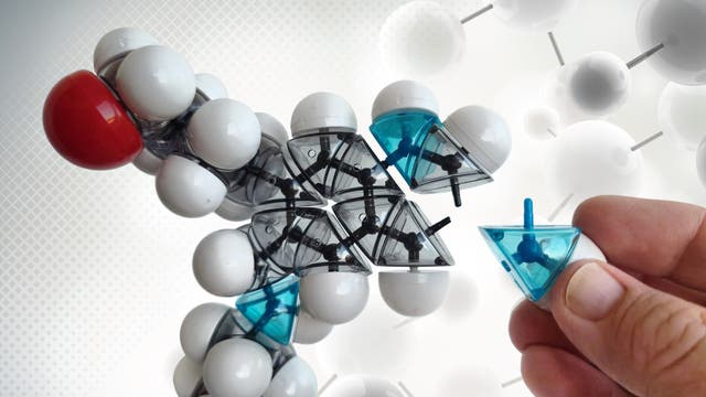 Ein Modell aus dem Molekülbaukasten, in das ein weiteres Atom eingefügt wird, vor einem abstrakten Hintergrund