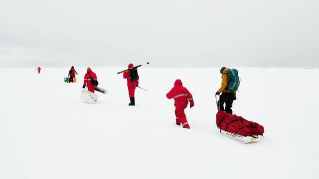 Menschen in roten Schneeanzügen stapfen durch Schnee