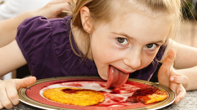 Kind schleckt Teller mit Pfannkuchen und Erdbeersoße