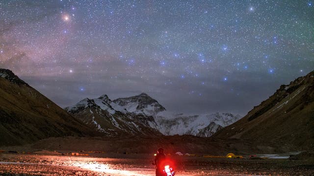 Der rötliche Antares im Sternbild Skorpion und die bläulichen Sterne des Centaurus leuchten über den hohen Berggipfeln des Himalaya. Der Motorrad-Tourist erreicht gerade das nördliche Basislager des Mount Everest in Tibet, das auf einer Höhe von 5170 Metern liegt.