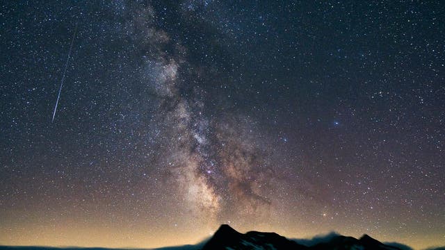 Ein Perseiden-Meteor vor der sternenreichen Milchstraße über der nächtlichen Alpenlandschaft.
