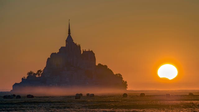 Die Klosterinsel Mont-Saint-Michel in der Normandie, eine Welterbestätte der UNESCO, bildete am 21. August 2017 eine malerische Kulisse für einen besonderen Sonnenuntergang. Teilweise vom Mond bedeckt, sank unser Tagesgestirn unter den Horizont.