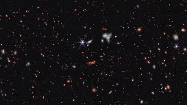 Ein tiefes Weltraumbild, das eine Vielzahl von Galaxien in unterschiedlichen Formen und Farben zeigt, die über das gesamte Bild verteilt sind. Einige Galaxien erscheinen als spiralförmige Strukturen, während andere als leuchtende Punkte oder diffuse Flecken sichtbar sind. Der Hintergrund ist schwarz, was die Helligkeit der Galaxien hervorhebt. Dieses Bild vermittelt die Weite und Vielfalt des Universums.