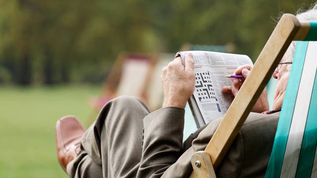 Älterer Mann löst Kreuzworträtsel im Gartenstuhl