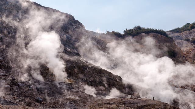 Dampfschwaden steigen von einem Hang aus dunklem vulkanischen Gestein auf