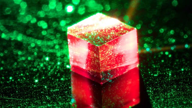 Ein würfelfürmiger Diamantkristall leuchtet rot unter grünem Laserlicht.