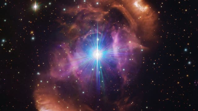 Diese Aufnahme im sichtbaren Licht des  VLT Survey Telescope zeigt im Zentrum einen hell leuchtenden Stern, der umgeben ist von einem farbigen kosmischen Nebel. Außerhalb des Nebels leuchten zahlreiche weitere Sterne in der Schwärze des Universums 