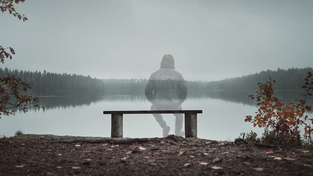 Halbdurchsichtige Silhouette eines Mannes, der auf einer Bank am See sitzt