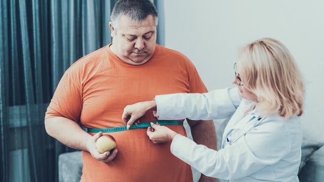 Eine Ärztin misst den Bauchumfang eines übergewichtigen Mannes.