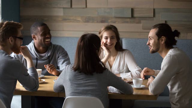 Eine Gruppe Freunde sitzt lachend und quatschend zusammen am Tisch 
