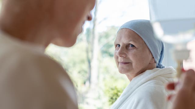 Eine offenbar an Krebs erkrankte Frau trägt ein Kopftuch und schaut hoffnungsvoll eine andere Frau an, die gerade einen Infusionsbeutel reguliert.