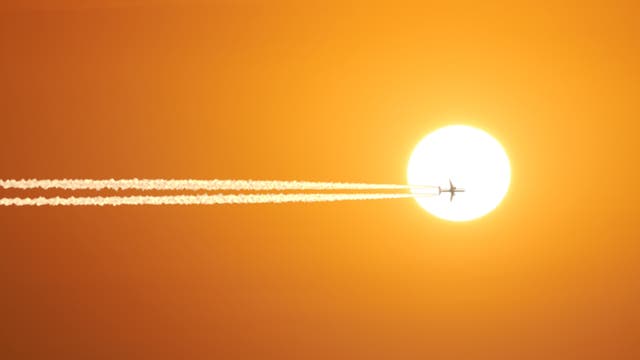 Ein Flugzeug mit Kondensstreifen vor der Sonne.