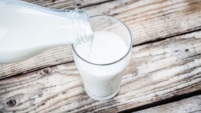 Milch wird aus einer altmodischen Glasflasche in ein Glas gegossen, das auf einem Holztisch steht.