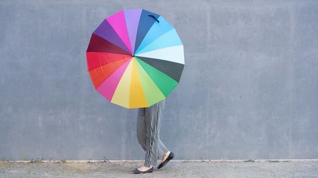 Mensch verdeckt hinter einem Schirm in Regenbogenfarben