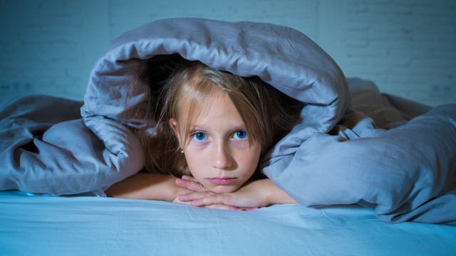 Ein Mädchen liegt im Bett und hat sich die Decke über den Kopf gezogen.