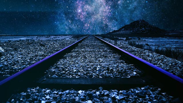 Verlassene Bahngleise führen unterm Sternenhimmel in Richtung Horizont
