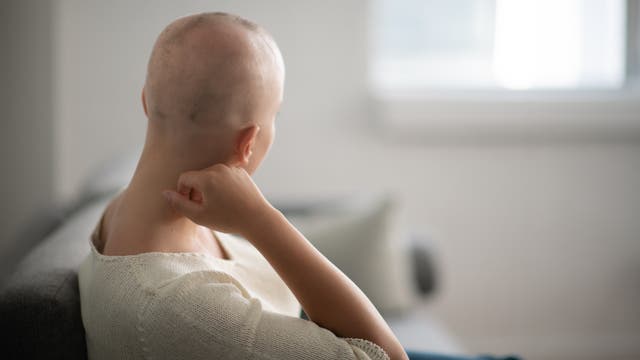 Krebskranke Frau sitzt auf Sofa und schaut aus dem Fenster