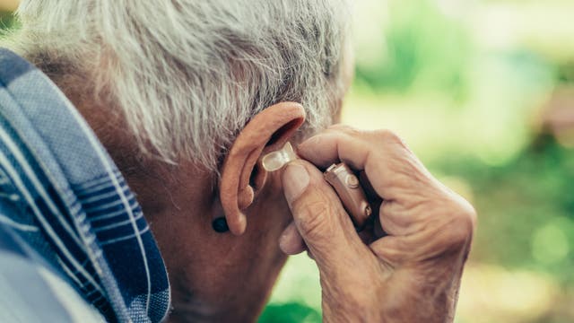 Ein älterer Mann setzt sein Hörgerät ein. 