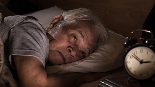 Älterer Mann liegt schlaflos im Bett und der Wecker zeigt drei Uhr morgens.