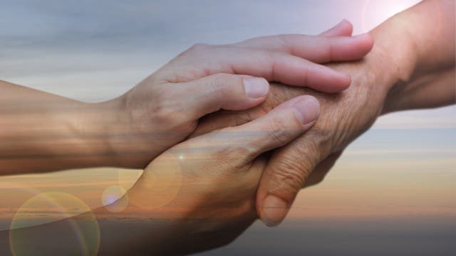 Nahaufnahme beider Hände einer jüngeren Person, die die Hand eines älteren Menschen halten