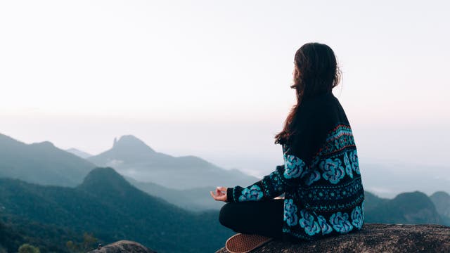 Eine Frau meditiert auf einem Gipfel mit Blick über die Berge