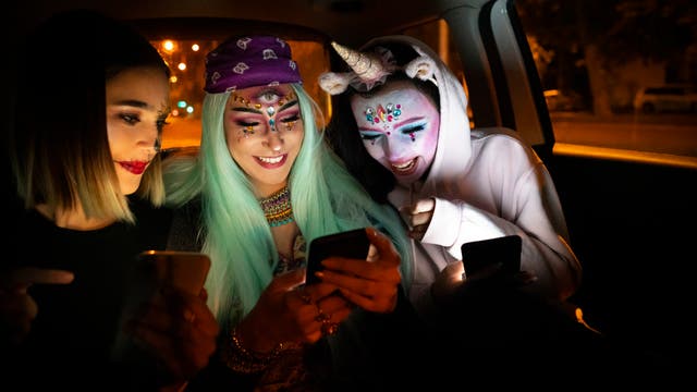 Drei junge Frauen auf dem Weg zur Kostümparty kommunizieren miteinander und dem Smartphone