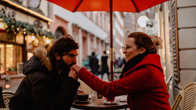Ein Mann hält und küsst die Hand einer Frau, während sie in einem Straßencafé sitzen