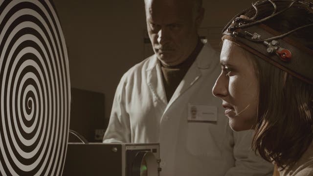 Frau mit Kabeln am Kopf schaut auf eine Spirale, beobachtet von einem Forscher