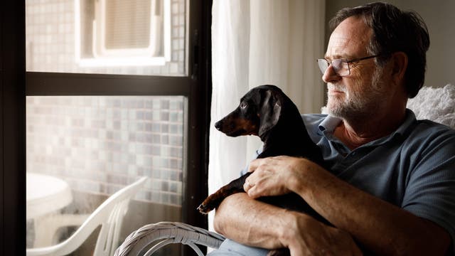 Älterer Mann mit Hund blickt nachdenklich aus dem Fenster 