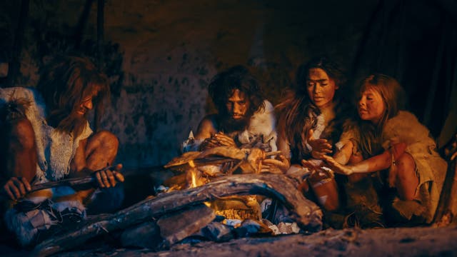 Prähistorische Jäger und Sammler tragen Tierhäute und essen Fleisch in einer Höhle in der Nacht