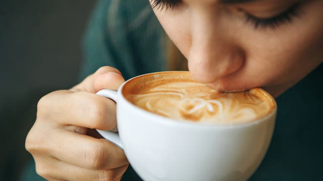 Nahaufnahme einer Frau, die eine Tasse Kaffee mit Milchschaum schlürft
