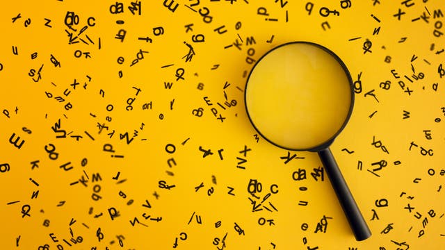 Ein schwarzes Vergrößerungsglas liegt auf einem gelben Hintergrund, umgeben von verstreuten schwarzen Buchstaben in verschiedenen Größen und Ausrichtungen. Das Bild vermittelt den Eindruck von Suche und Entdeckung, wobei der Fokus auf den Buchstaben liegt, die durch das Glas vergrößert erscheinen.