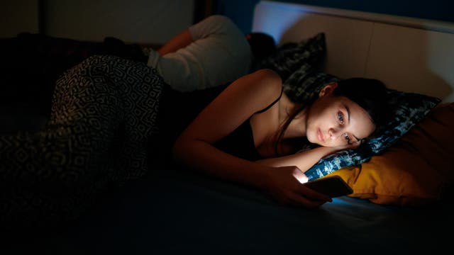 Frau liegt im Bett und spielt am Smartphone