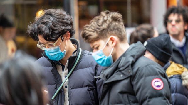 Zwei Junge Männer mit Mundschutz gucken auf ihre Handys, um den neuesten Spektrum-Artikel über das Coronavirus zu lesen.