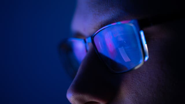 In einer Brille spiegelt sich blaues Licht eines Computermonitors