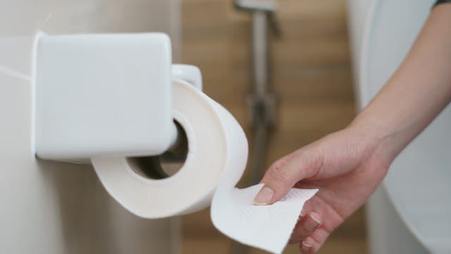 Eine Hand reißt ein Blatt von einer Klopapierrolle ab 