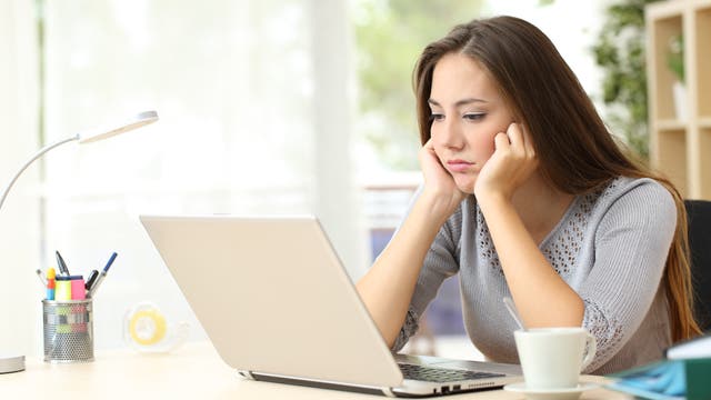 Eine Frau sitzt vor ihrem Laptop, mit traurigem Gesichtsausdruck.