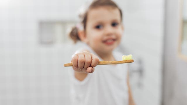 Ein Mädchen hält im Badezimmer in seiner ausgestreckten Hand eine Zahnbürste.