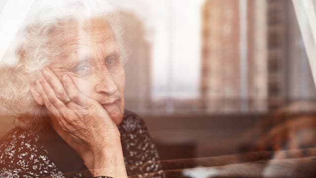 Eine ältere Frau blickt aus dem Fenster ihrer Wohnung.