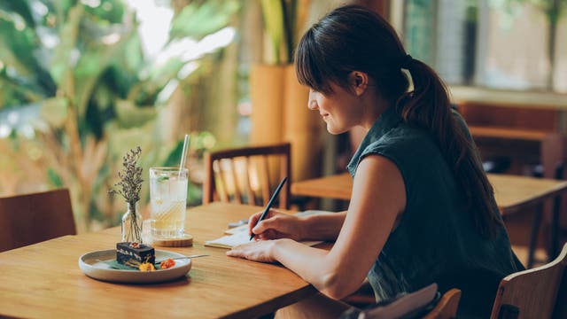 Frau sitzt in einem Café am Tisch und schreibt etwas