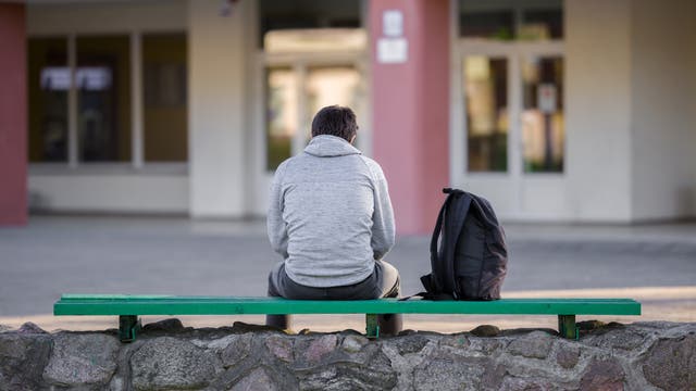 Ein Jugendlicher sitzt auf einer Bank auf dem Schulhof. (Symbolbild)
