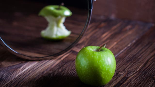 Ein vollständiger grüner Apfel erscheint im Spiegel als abgenagter Apfel