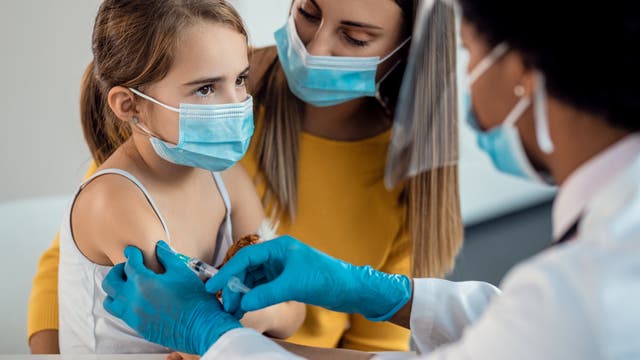 Ein Kind mit Maske wird von einer Ärztin geimpft