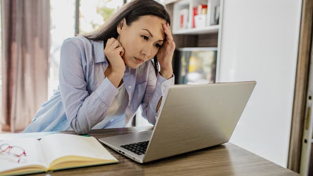 Eine Frau blickt müde auf ihren Laptop-Bildschirm.