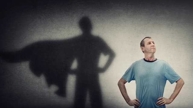 Mann im T-Shirt vor einer Wand; sein Schatten zeigt ihn mit Heldencape.