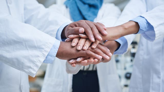 Menschen in Laborkitteln legen Hände übereinander und signalisieren Zusammenhalt